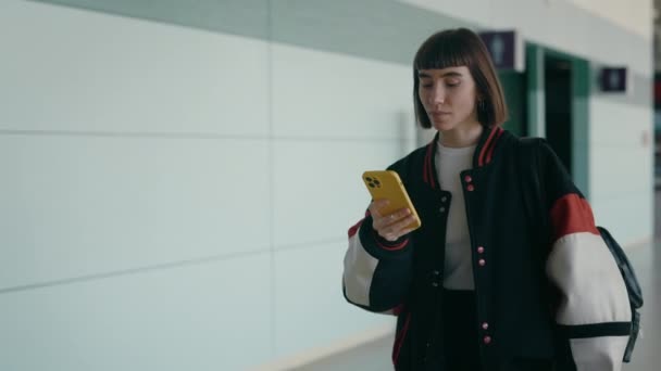 Femme en blouson de bombardier marchant à l'aéroport avec smartphone — Video