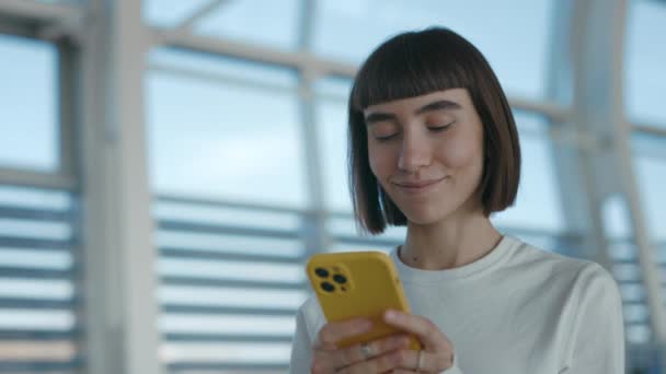 Mujer sonriente utilizando el móvil para el chat en línea en el aeropuerto — Vídeo de stock