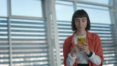 Modern havaalanında akıllı telefonlu sevimli bir kadın yürüyor.