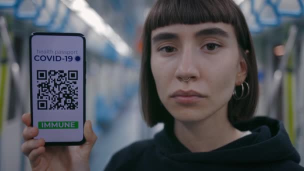 Vista retrato da mulher de cabelos curtos perfurada olhando calmamente para a câmera e mostrando passaporte da vacina em seu smartphone — Vídeo de Stock