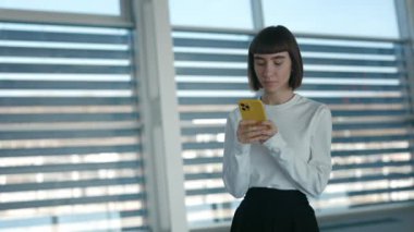 Havaalanında dikilirken cep telefonunda mesaj yazan kadın