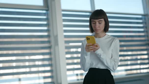 Vrouw typt berichten op mobiel terwijl ze op de luchthaven staat — Stockvideo