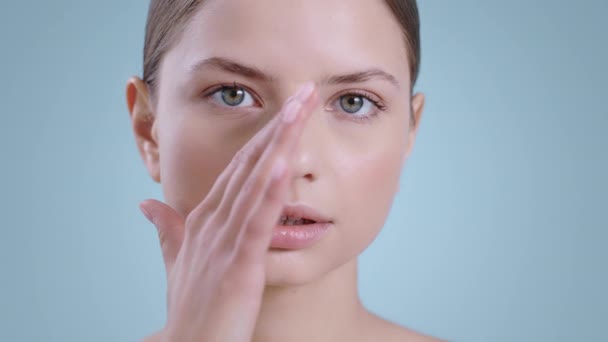 Gros plan d'une jolie femme touchant le visage d'une main tout en regardant la caméra. Portrait d'une femme nue qui pose. Concept de cosmétologie, soins de la peau. — Video