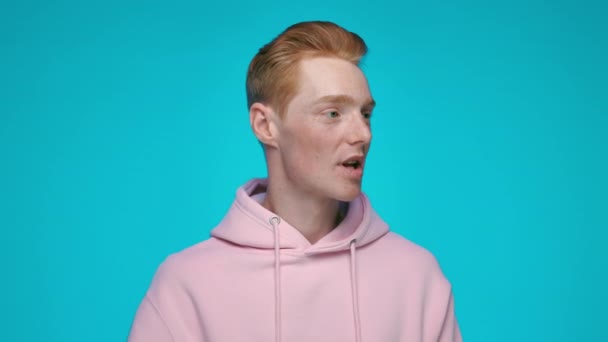 Érzelmes vörös hajú férfi rózsaszín kapucnis pulcsiban kiabál hangosbeszélőben — Stock videók
