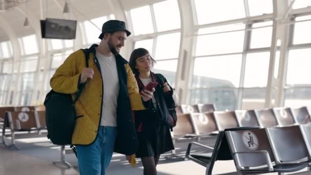 Paar geht mit Handy gemeinsam am Flughafen spazieren — Stockvideo