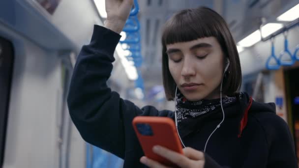 Atrakcyjna kobieta korzystająca z telefonów komórkowych i słuchawek w metrze — Wideo stockowe