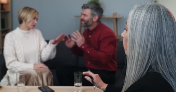 Woman psychologist calming down married couple that discussing family problems and shouting on each other while sitting on couch. Husband and wife arguing while having therapy session. — Stock Video
