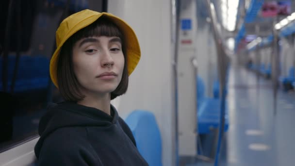 Frau mit gelbem Eimer-Hut sitzt in leerer U-Bahn — Stockvideo
