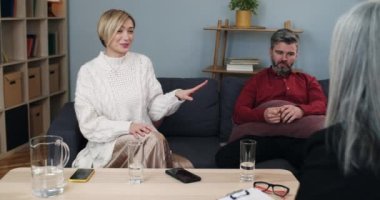 Psikologlarda kanepede oturan beyaz bir çift. Bir kadın evlilik sorunlarını paylaşırken kocasına gülüp, gösteriş yapıyor ve elinde not panosuyla danışman ile konuşuyor..