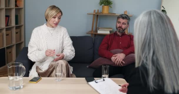 Beskär syn på man och kvinna diskuterar familjeproblem med psykolog. Kvinnan pratar och hennes man lyssnar under terapisessionen med specialisten. Begreppet förhållande. — Stockvideo