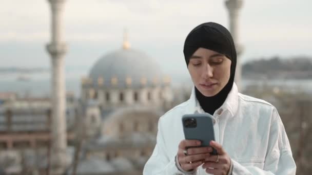 Perempuan berjilbab berjalan di jalan dengan smartphone di tangan — Stok Video