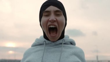 Portrait of woman in hijab screaming with anger outdoors