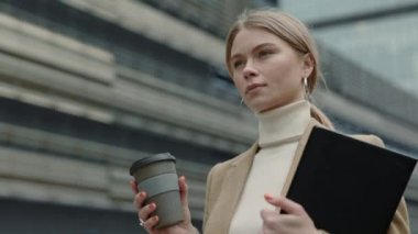 İş elbiseli bir kadın şehirde elinde kahve ve pano tutuyor.