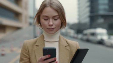 İş elbiseli kadın sokakta yürürken cep telefonu kullanıyor.