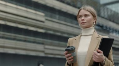 İş kadını elinde dosya ve kahveyle sokakta yürüyor.