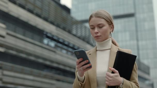 Señora llevando portapapeles y móvil en las manos al aire libre — Vídeos de Stock