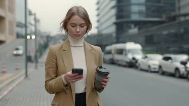 İş kadını elinde kahve ve cep telefonuyla işe gidiyor.