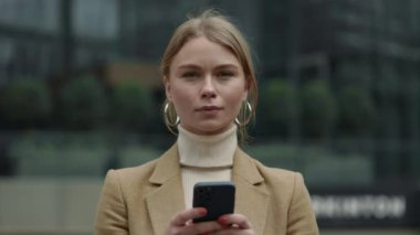 İş kadını sokakta dikiliyor ve akıllı telefon kullanıyor.