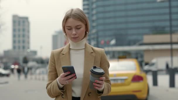 Wanita cantik dalam pakaian formal menggunakan ponsel dan membawa kopi — Stok Video