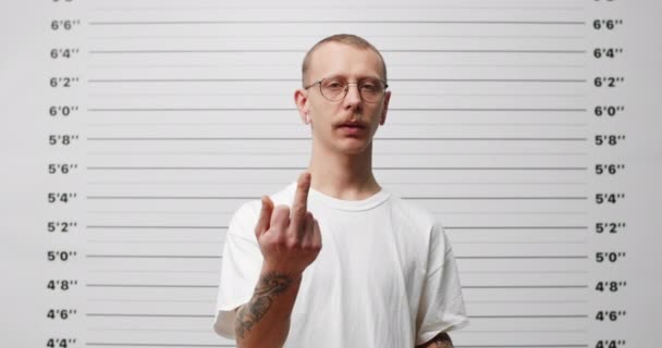 Lviv, Ukraine - December 21, 2019: Man with tattoos on his arm put down sign for photo in police department. Young man with mustaches showing middle finger fuck gesture while looking to camera. — Stok video