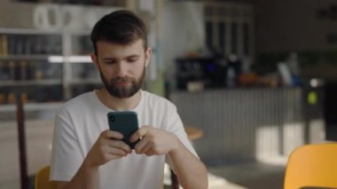 Kafe masasında oturan ve akıllı telefon kullanan yakışıklı adam.