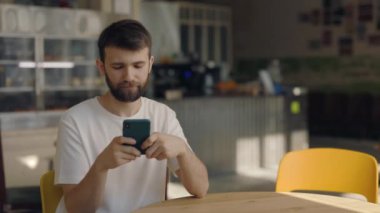 Kafede cep telefonuyla internette sörf yapan neşeli sakallı adam.