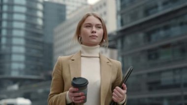 İş kadını elinde dosya ve kahveyle sokakta yürüyor.