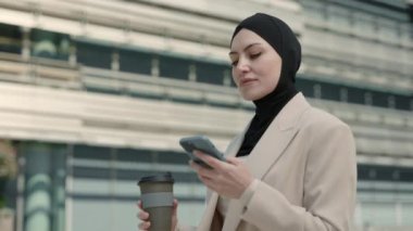 Cep telefonu ve kahveyle gezen Arap bir kadın.