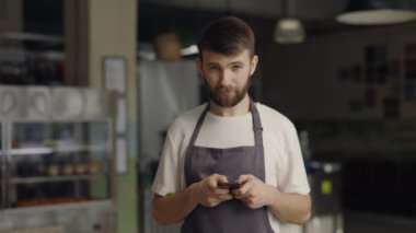 Kafe 'de akıllı telefon kullanan önlüklü beyaz garson.