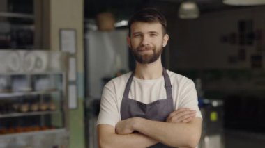 Dost canlısı erkek barmen, kafede kollarını kavuşturmuş poz veriyor.