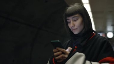 Metroyu beklerken akıllı telefon kullanan çekici bir kadın.