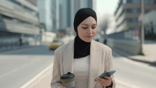 Женщина в хиджабе с помощью мобильного телефона и пить кофе на открытом воздухе — стоковое видео