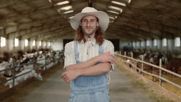 Jeune homme en uniforme de travail debout à la ferme avec des chèvres — Video