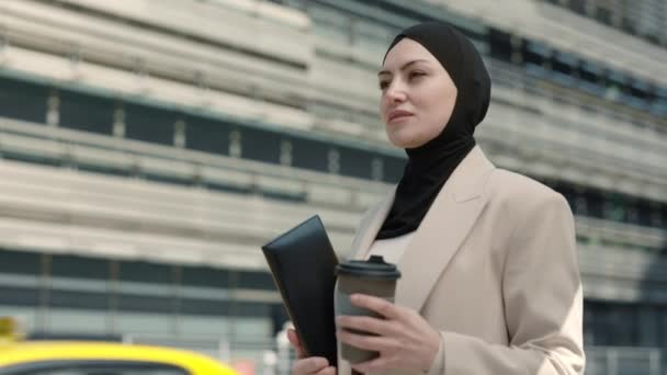 Exitosa señora árabe llevando café y portapapeles al aire libre — Vídeo de stock