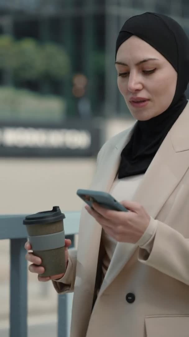 Verticale video. Zakelijke vrouw in hijab lopen met mobiele telefoon in handen — Stockvideo