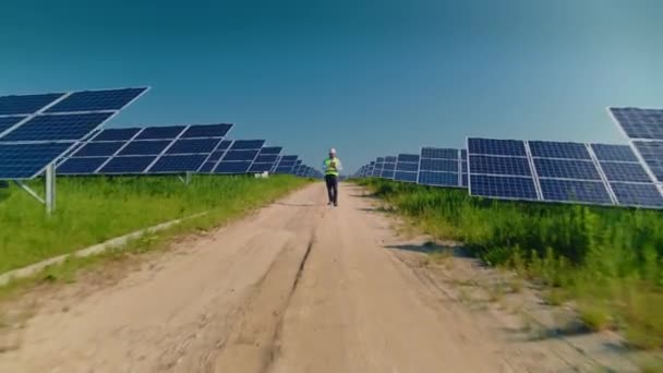 Aurinkosähkölaitoksen työntekijä, joka valvoo lennokkia pellon yllä — kuvapankkivideo