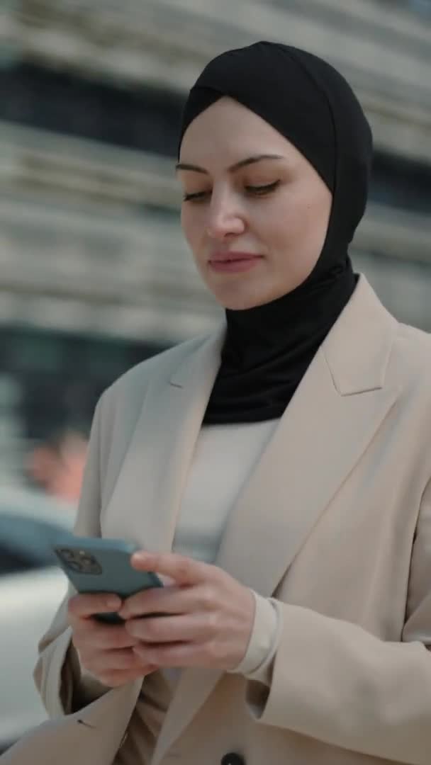 Vídeo vertical. Señora de negocios en hijab escribiendo mensajes en el móvil al aire libre — Vídeos de Stock
