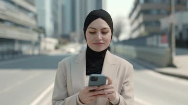 İş kadını tesettürde yürürken cep telefonu kullanıyor.