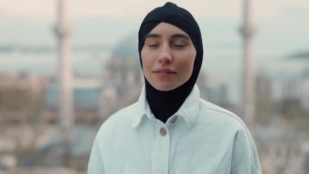 Portrait of beautiful muslim woman looking to the camera in black hijab on on the background of the mosque. Youth culture and lifestyle concept. — Stock Video