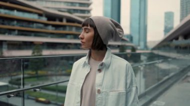 Sıradan giyinmiş bir kadın alışveriş merkezinin yakınındaki kameraya bakıyor.