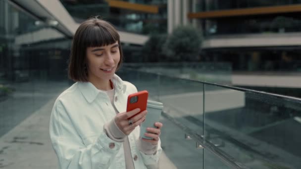 Haberler iyi. Mobil ekrana bakıp "Vay canına" diyen duygusal genç bir kadın. Güzel esmer, alışveriş merkezinin yanında duruyor. Başarılı alışverişin keyfi. — Stok video
