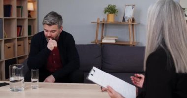 Düşünceli olgun bir adamın kanepeye oturup bir kadınla terapi seansı yapması. Kadın psikolog konuşurken ve not alırken erkek sakallı insan dinliyor..
