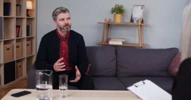 Sakallı adamın kadın psikologla rahat bir ofiste görüşü. Kadın terapist notlar alırken erkek yakışıklı konuşuyor ve el kol hareketi yapıyor. Ruh sağlığı kavramı.