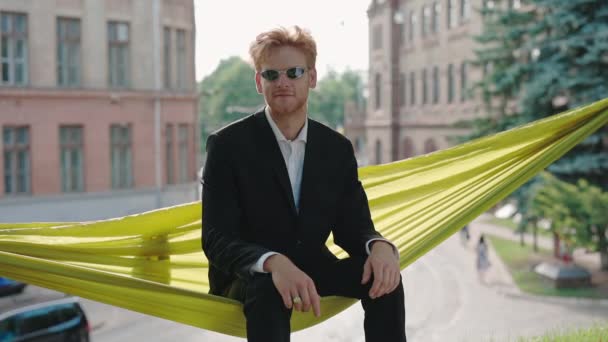Joven inteligente en traje y gafas sentado en hamaca — Vídeos de Stock
