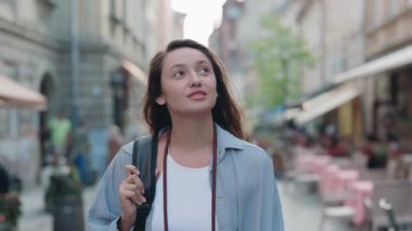 Sırt çantalı pozitif kadın turist şehir sokaklarında yürüyor.