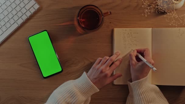Mujer escribiendo en planificador y utilizando el móvil con pantalla verde — Vídeo de stock