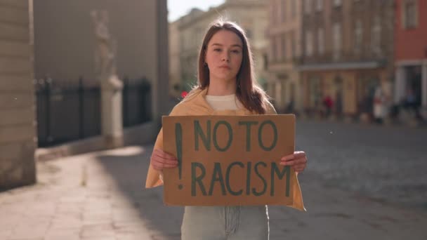 Женщина, держащая знамя "Нет" расизму на городской улице — стоковое видео
