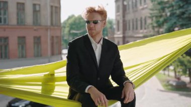 Takım elbiseli ve hamakta dinlenen güneş gözlüklü bir iş adamı.