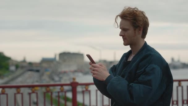 Pelirroja chico escribiendo mensajes en el teléfono inteligente al aire libre — Vídeos de Stock