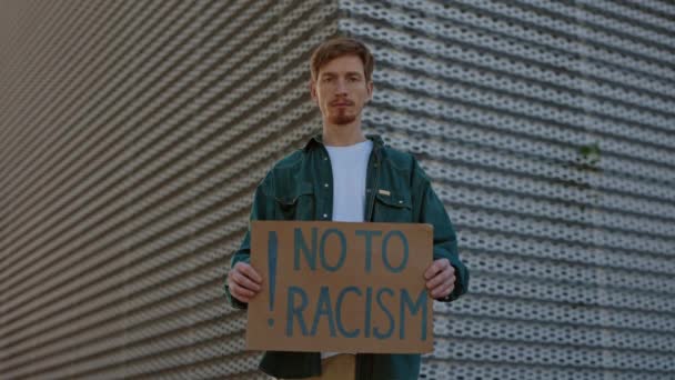 Человек, держащий плакат с фразой "нет" расизму на улице — стоковое видео